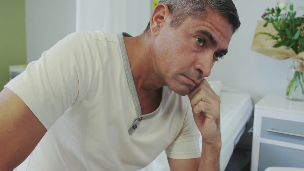 Vista frontale di un paziente maschio caucasico pensieroso che guarda altrove nel reparto ospedaliero 4K