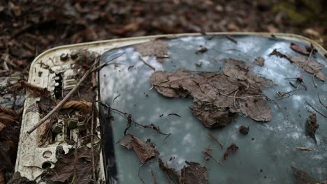 old white crt tv half covered with leaves abandoned in the woods, close up shot