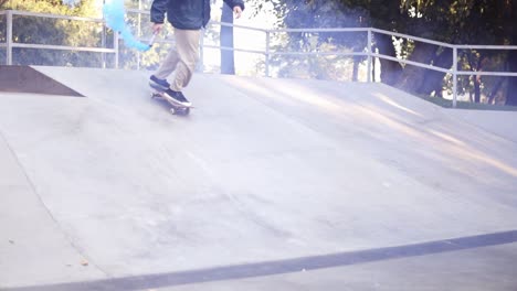 young guy practicing air tricks during summer day while holding blue coloured burning smoke bomb on the skate ramp