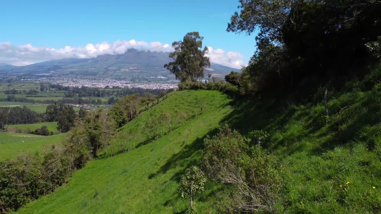 Drone flight on the sunny side of a green hill with the view on the El corazón volcano in Ecuador on a sunny day with blue sky, copy space