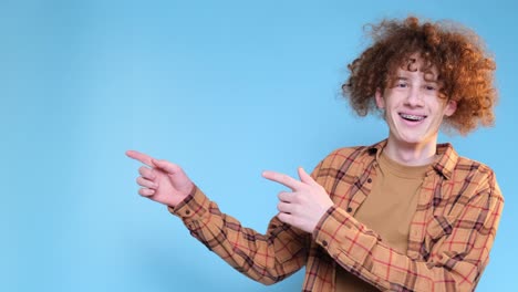 curly redhaired student on a beautiful blue background is posing and gesturing with his hands curly redhaired student on a beautiful blue background is posing and gesturing with his hands advertising shooting in the studio