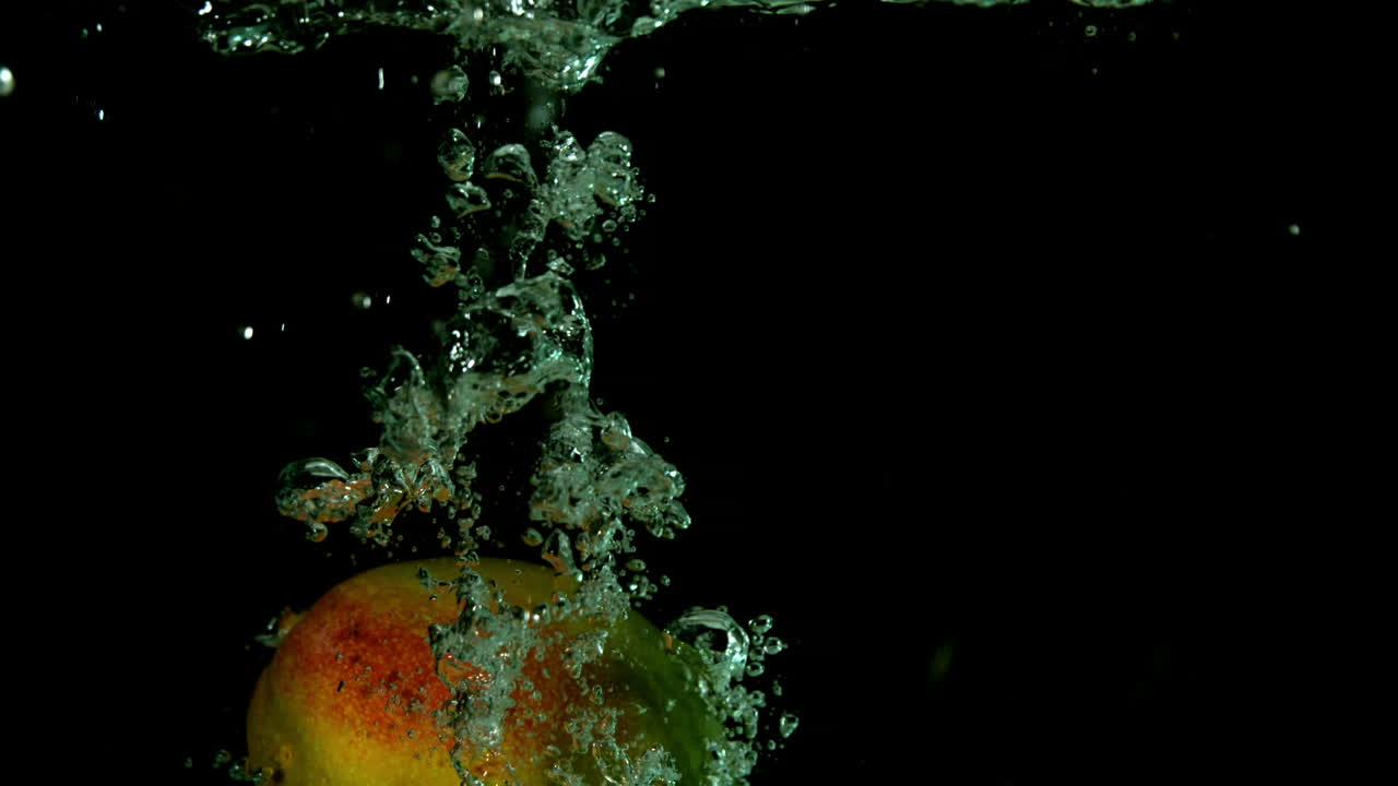 mango cayendo en el agua sobre un fondo negro