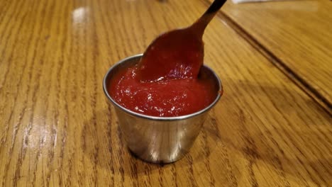 agitando la salsa de pizza en un tazón de acero inoxidable con una cuchara de plata en una mesa de madera