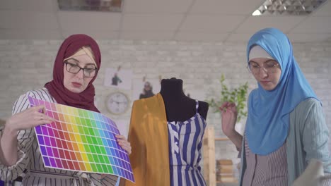 young muslim women fashion designers in national headscarves in a modern studio engaged in fitting on a mannequin close up