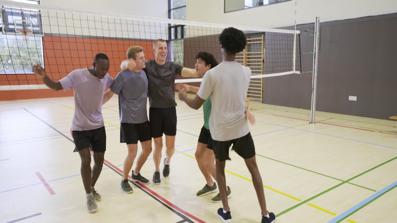 Diverses Männerteam feiert hüpfend im Fitnessstudio nach einem Punktgewinn, geht zur Bank mit Volleyball in Sportkleidung.