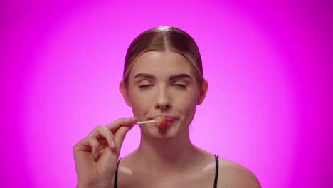 portrait woman looking at camera and licking confectionary lollipop, studio