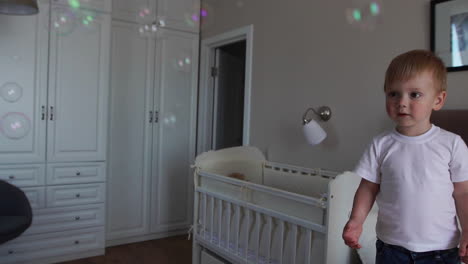 a boy in a white t-shirt and blue jeans catches soap bubbles standing on the bed in the parent bedroom