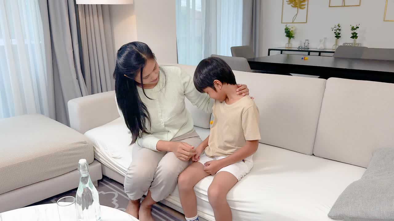 Mother gently consoles her upset son in a bright, modern living room with soft lighting
