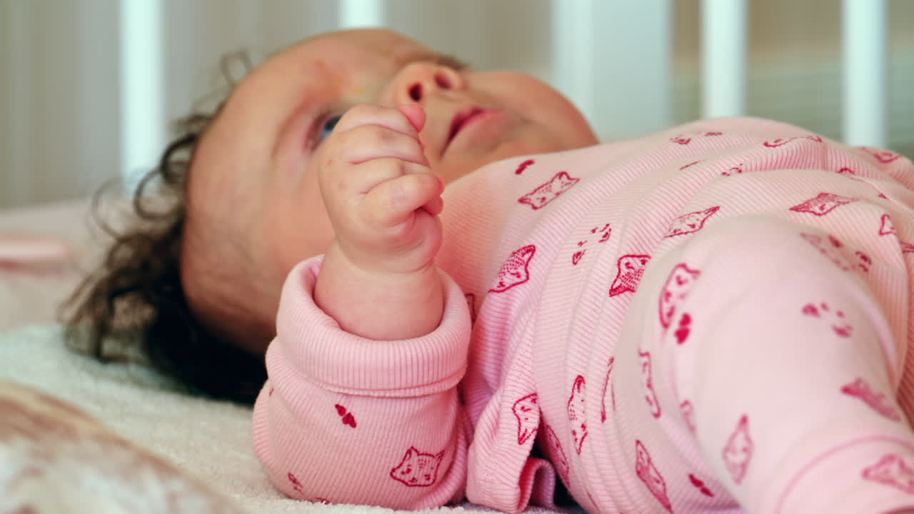 Primo piano di un bambino sereno che dorme in una culla, indossando un completino rosa.