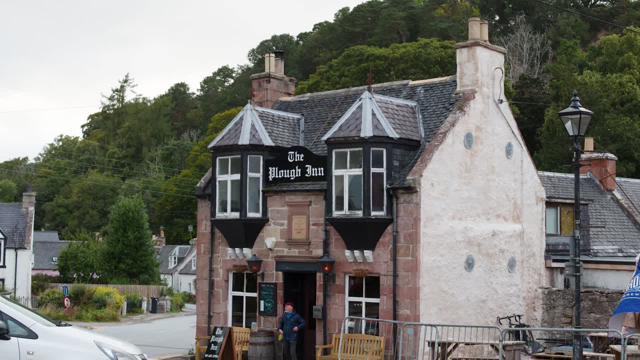 A man leaves a traditional stone inn on a cloudy day in Rosemarkie, Scotland