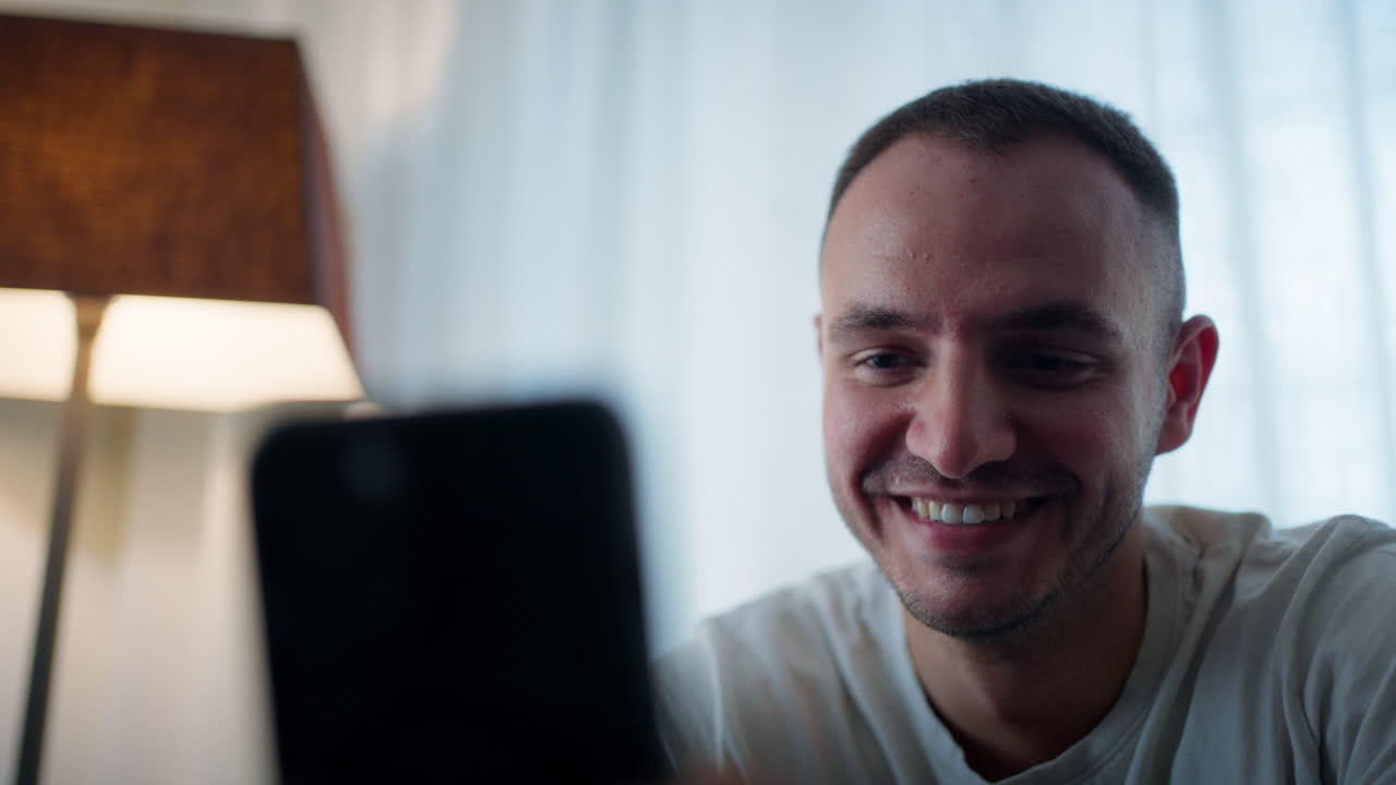 Young man bored in living room looking at phone, feeling apathetic