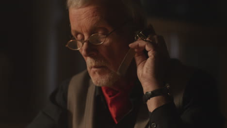 older passionate man evaluates an old watch in his office at night