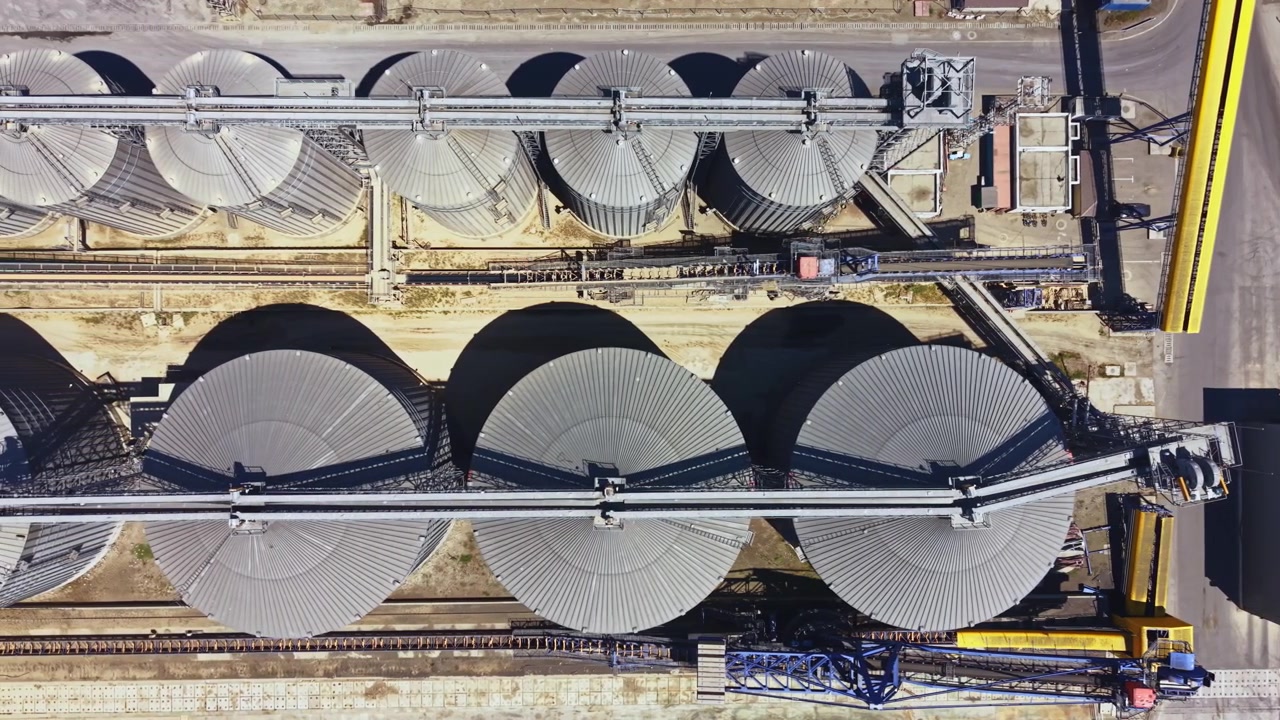 Grandi silos di stoccaggio e macchinari in un'area industriale gestiscono l'approvvigionamento di grano in un sito di lavorazione durante il giorno.
