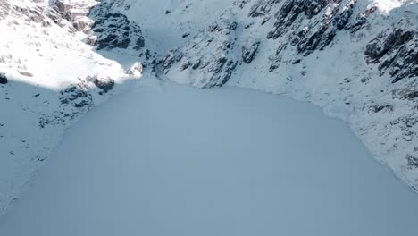 aerial of frozen alpine lake at foot of rugged, snowy mountains, campagneda, italy