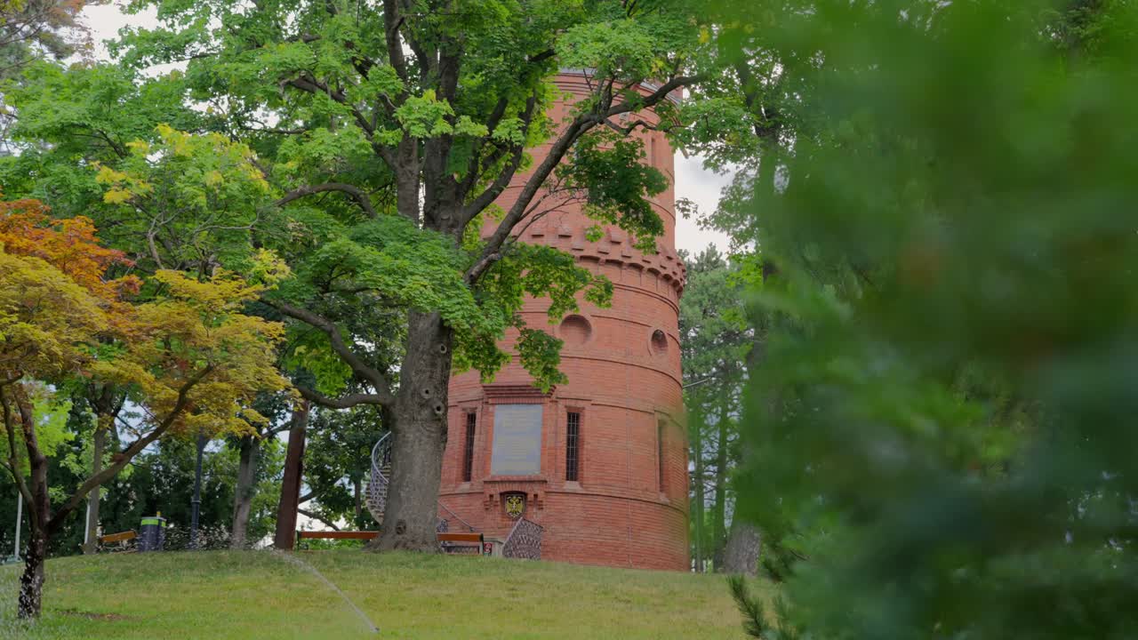 Medium shot of Aussichtsturm Paulinenwarte in T&uuml;rkenschanzpark in Vienna with a blurry leaves in the foreground, water sprinklers surrounded by trees during a sunny day at noon