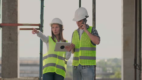 Building-in-construction-with-a-female-and-a-male-builders-constructors-engineers-walking-along-it