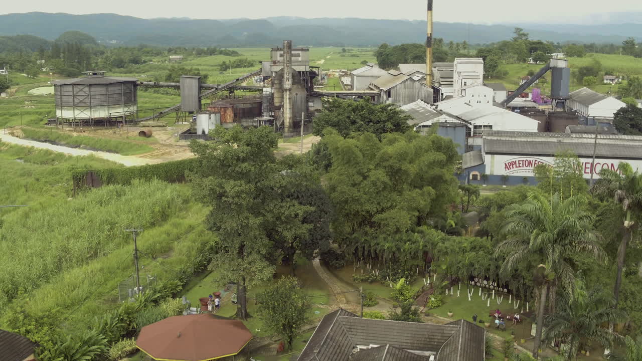 Luchtfoto van het Appleton rum landgoed, dat omhooggaat om de bewegwijzering op het gebouw, de uitgestrektheid en de schaal van het terrein te onthullen, terwijl een zwerm vogels onderin beeld vliegt