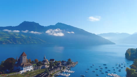 satisfying drone flyover of boats in pier on picturesque lake near medieval church in spiez, switerzland in the summer, noon, wide view, europe