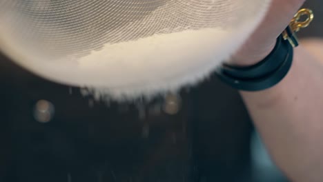 woman gradually strains flour through fine sieve closeup