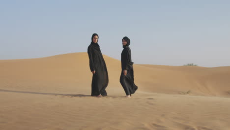 dos hermosas mujeres musulmanas en hiyab de pie en un desierto ventoso y sonriendo a la cámara 2