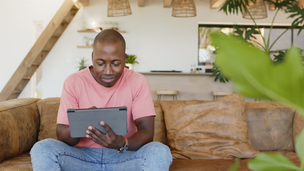 Sitting on couch, man using tablet and smiling in modern living room