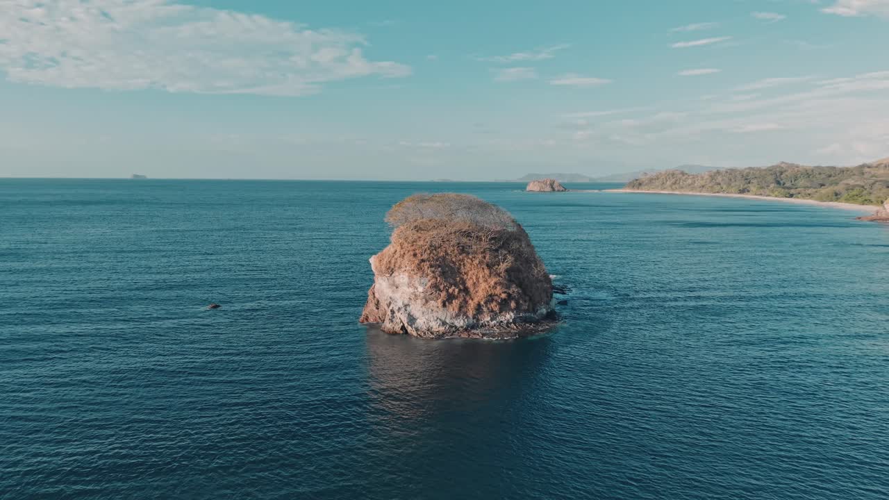 Aerial zoom in showing Bahia Los Piratas beach with vibrant ocean colors and rocky coastline in Costa Rica
