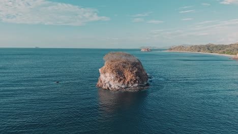 aerial zoom in showing bahia los piratas beach with vibrant ocean colors and rocky coastline in costa rica