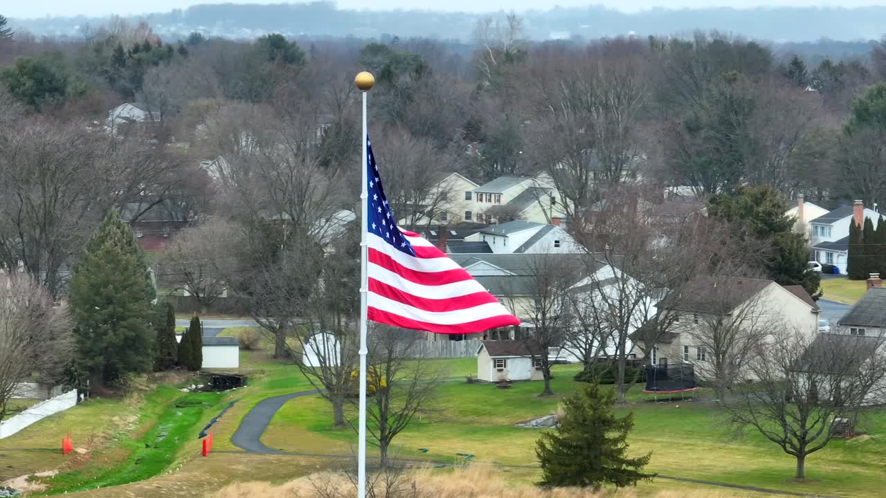 primer plano aéreo de la bandera estadounidense ondeando sobre el vecindario suburbano