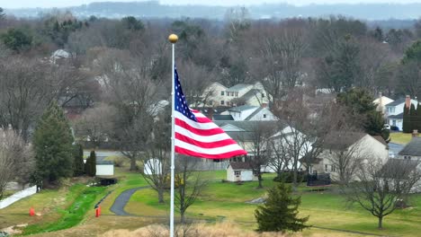 aerial close up of american flag waving over suburban neighborhood