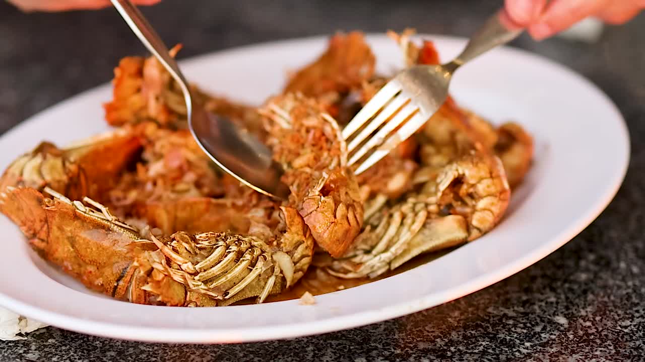 Close-up of crispy mantis shrimp being enjoyed with utensils on a white plate.