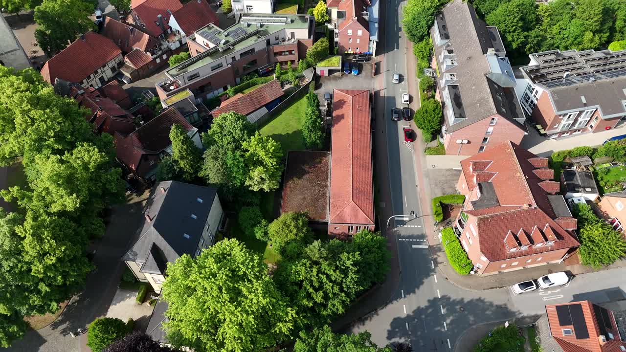 Driving cars on street of historic old town in Germany at sunny day. Aerial tracking shot. Orange tile and red brick houses and villas in small city. Top down. Summer day with green trees.