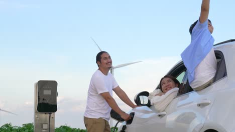 concept of progressive happy family at wind farm with electric vehicle.