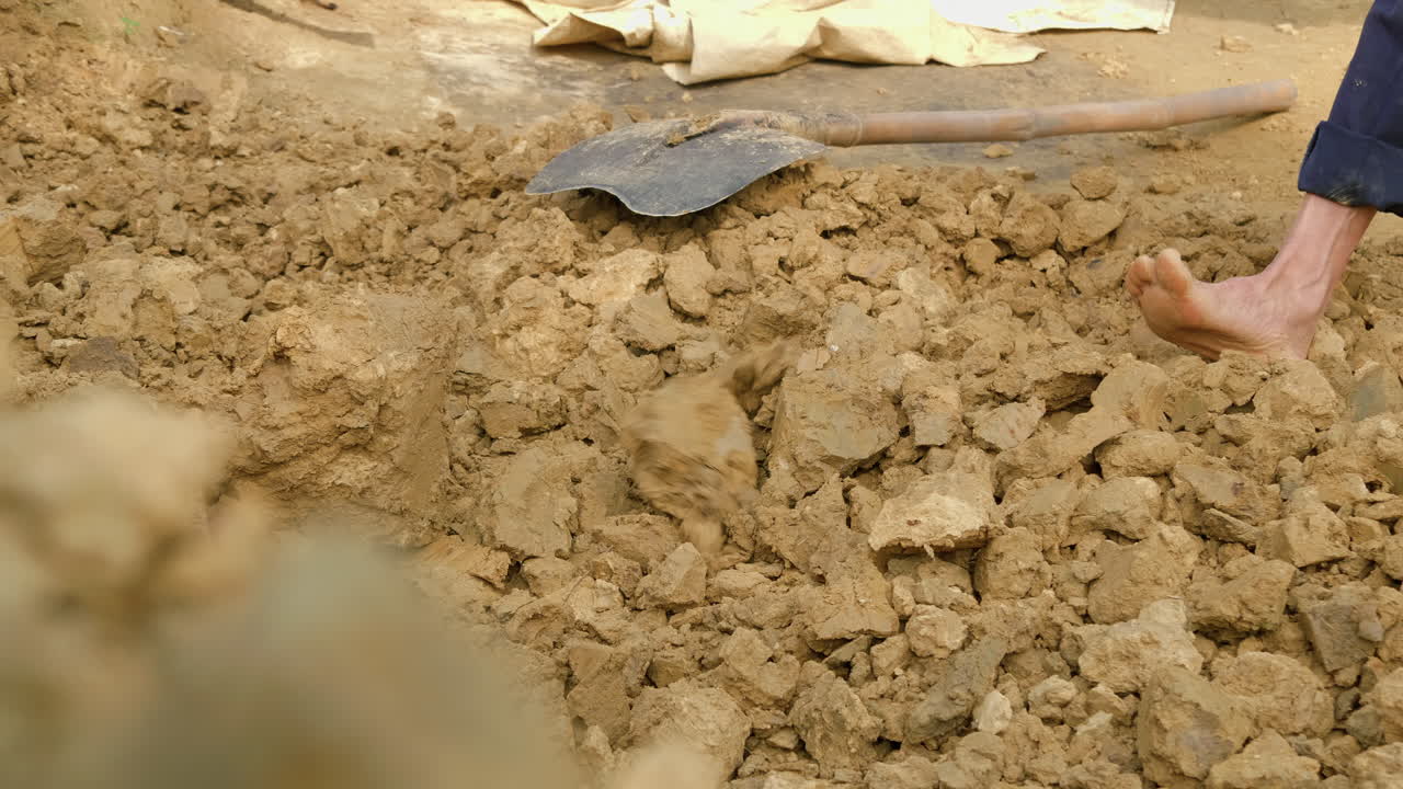 맨발의 남자는 괭이를 사용하여 전통 도자기를 위한 새로운 점토 토양을 수집하여 천연 자원과 문화 유산의 중요성을 보여줍니다.
