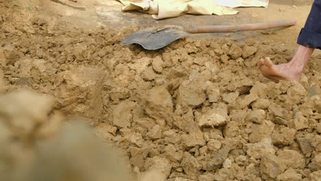 a barefoot man uses a hoe to collect new clay soil for traditional pottery, showcasing the importance of natural resources and cultural heritage
