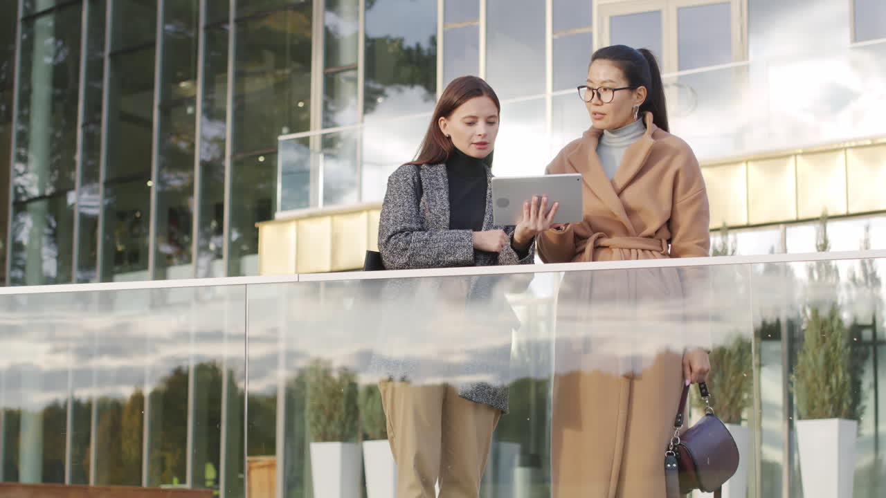 Two businesswomen discussing with a tablet outside a modern office building