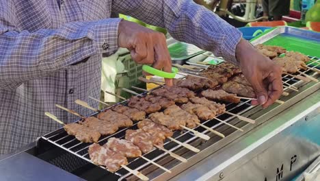 street food vendor preparing grilled meat skewers