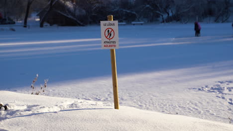 sign warning people to not step on ice with people on ice in background