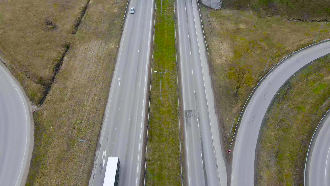 Top down aerial drone footage flying over Tallinn Pärnu highway where cars, trucks and vehicles drive on a cloudy day. Video also shows a bridge crossing the highway, brown and green grass around it.