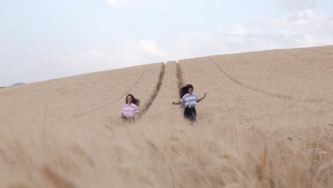 two young female friends enjoying the nature together while walking in a wheat field.