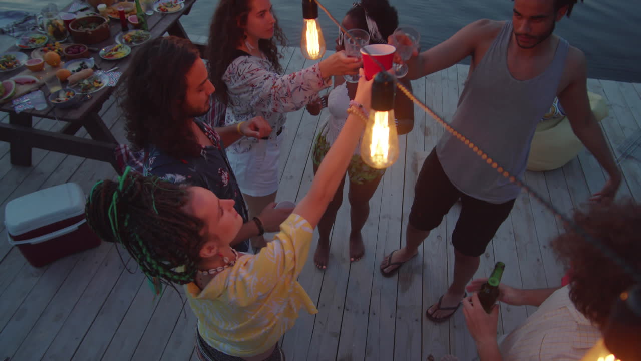 amigos brindando con bebidas y bailando en la fiesta del lago