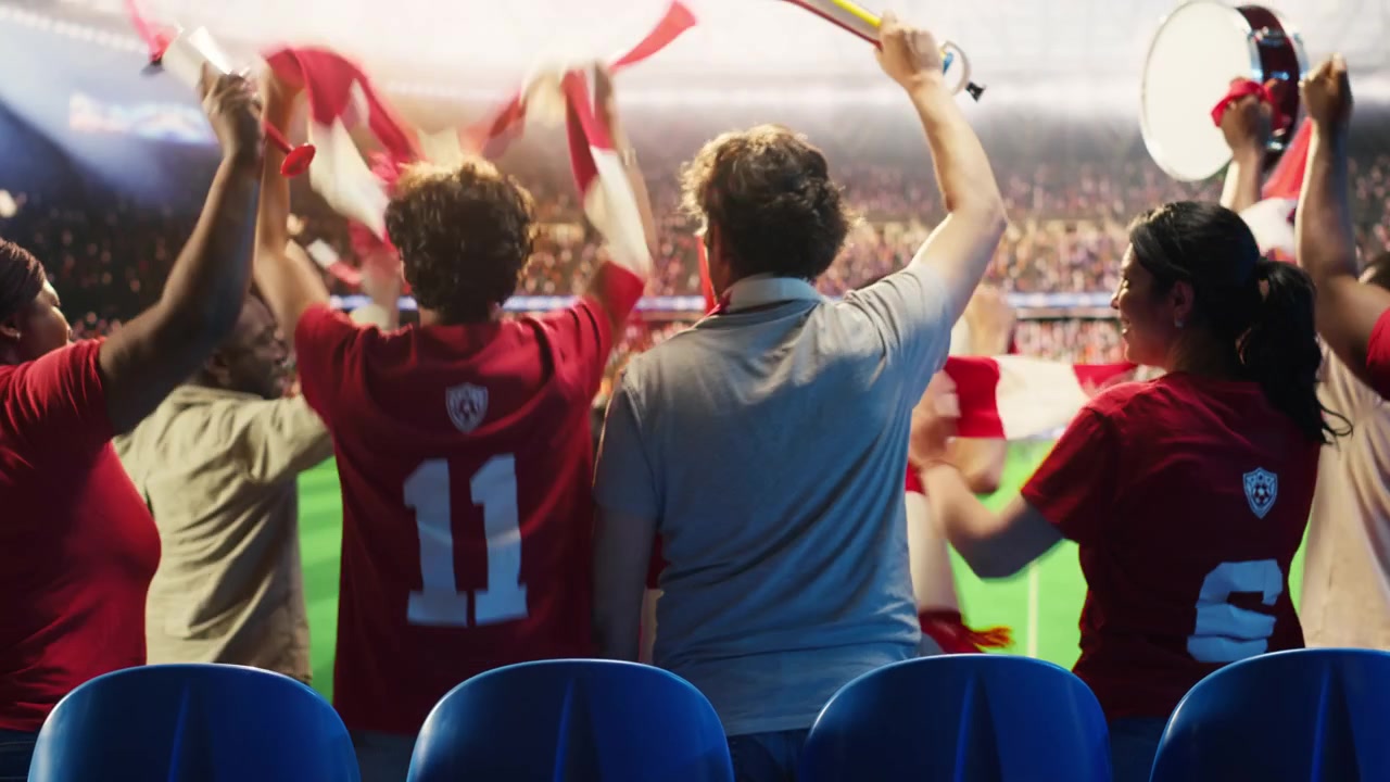 Aficionados al fútbol con camisetas rojas tocan vuvuzelas, caminando en el estadio