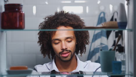 View-Through-Bathroom-Cabinet-Of-Young-Man-Getting-Ready-For-Work-And-Moisturizing-Skin