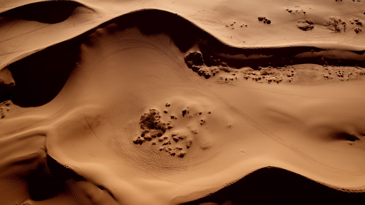 Surreal drone imagery showcases the flowing forms and vivid tones of pink sand dunes below.
