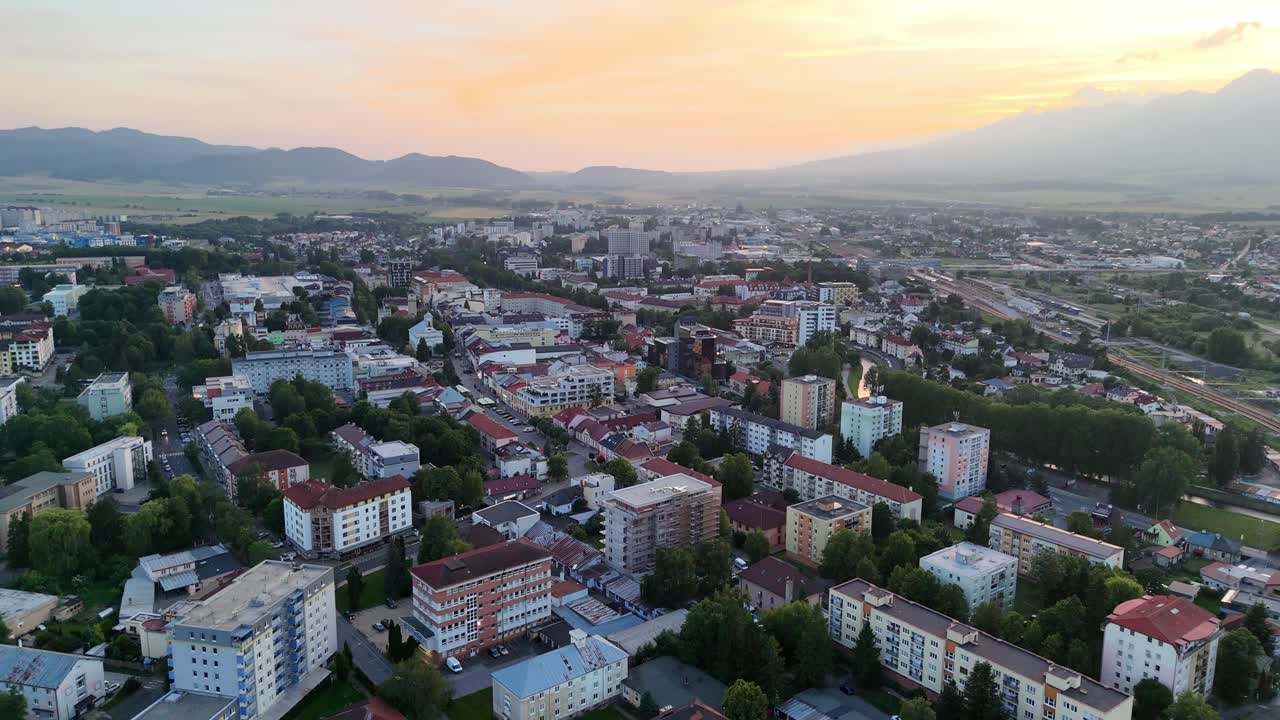 Aerial view of Poprad city at sunset, with warm evening light over urban buildings and distant mountains in soft haze