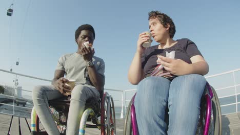 Happy couple using wheelchairs eating and talking outdoors