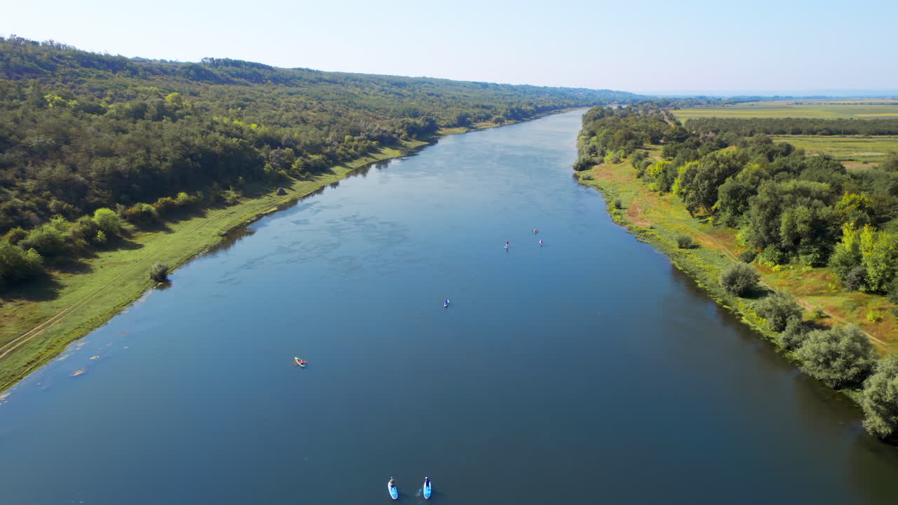 Vista aerea con drone di più persone che fanno stand-up paddleboarding sul Dniester in Moldova. Lussureggiante foresta su entrambi i lati del fiume