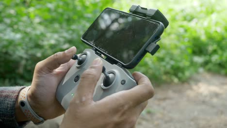primer plano de la mano del piloto de drones usando el control remoto de drones dji con un teléfono inteligente conectado en un paisaje forestal para la vigilancia de la vida silvestre, india