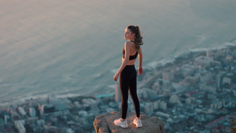 young woman with arms raised on mountain top celebrating achievement girl on edge of cliff looking at beautiful view at sunset enjoying travel adventure