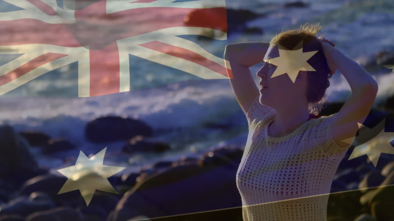 Standing by rocky shore, woman with Australian flag animation in background