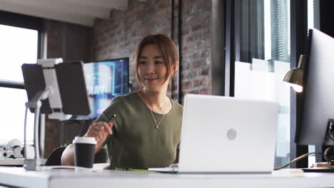 asian businesswoman in a modern office gives a thumbs-up, with laptops and monitors around her